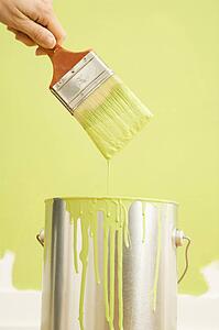 Female hand holding paintbrush over paint can