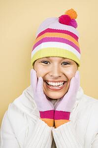 Young adult woman wearing winter hat and gloves with hands to face smiling at viewer