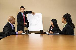 Businesspeople sitting at conference table while businessman gives presentation