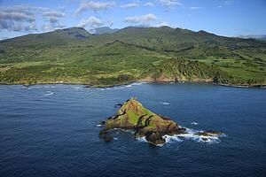 Aerial of rock jutting out of Pacific ocean off the coast of Maui, Hawaii with mountain landscape in background