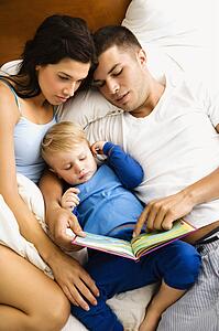 Caucasian parents and toddler son reading book in bed.