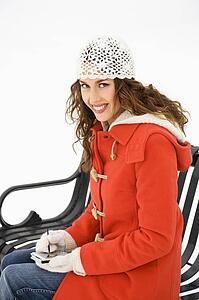 Caucasian young adult female in winter clothing sitting on park bench using PDA and smiling at viewer.