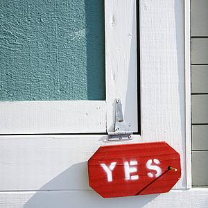 Detail of exterior wooden door on building with sign reading yes.