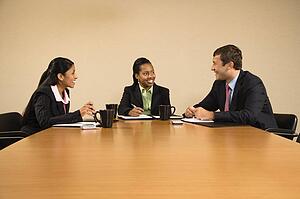 Businesspeople sitting at conference table talking and smiling.
