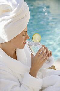 Mid-adult woman wearing robe and towel on head drinking from glass next to pool