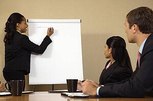 Businesspeople sitting at conference table while businesswoman gives presentation