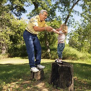 Grandfather and granddaughter playing outside holding hands balancing on stumps
