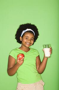 Girl holding glass of milk and apple