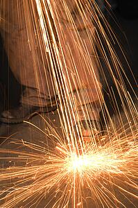 Caucasian male metalsmith shaping metal and creating sparks.