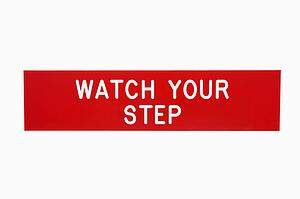 Red sign reading watch your step against white background.