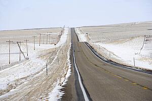 Road over rolling hill landscape with snow and power lines