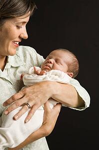 Mother smiling holding baby against 