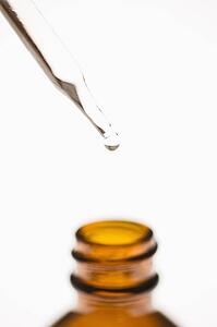 Dropper placed above brown bottle with white background.