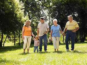 Family holding hands walking across grass in park smiling
