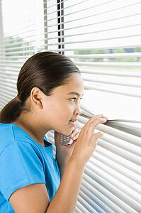 Girl looking through blinds out window