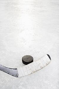 Close up of ice hockey stick on ice rink in position to hit hockey puck.