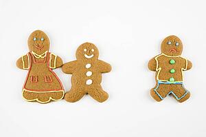 Frowning male gingerbread cookie standing separate from happy gingerbread cookies holding hands.