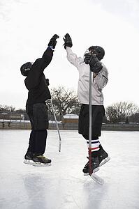 Two boys in ice hockey uniforms giving eachother high five on ice rink.
