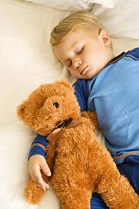 Toddler boy sleeping in bed with teddy bear