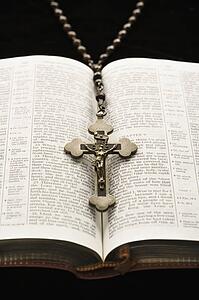 Rosary with crucifix lying on open Bible.