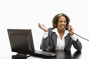 Businesswoman sitting at office desk with computer talking on telephone looking upset