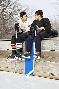 Two boys in hockey uniforms sitting on ice rink wall