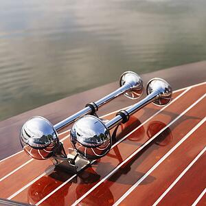 Detail of dual chrome trumpet horns on wooden boat floating in water.