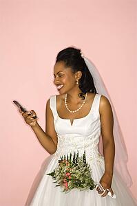 Mid-adult African-American bride looking at cellphone on pink background. 