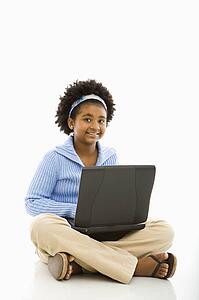 Girl sitting on floor using laptop and smiling at viewer
