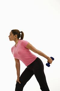 Side view of mid adult woman wearing pink shirt exercising with dumbbell.