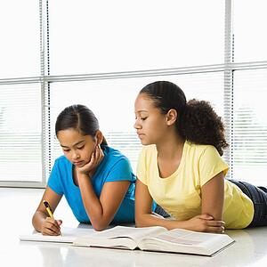 Two preteen girls lying on floor doing homework together.