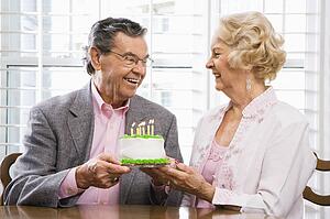 Mature Caucasian couple holding birthday cake looking at each other.