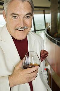 Mature Caucasian man in suit holding snifter of brandy smiling.