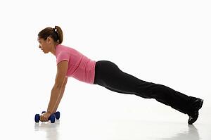Side view of mid adult woman wearing pink exercise shirt doing pushups while holding dumbbells.