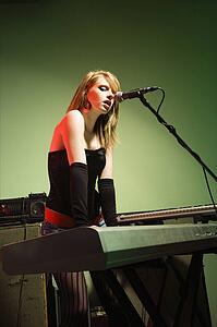 Caucasian female singing into a microphone and playing the keyboard.