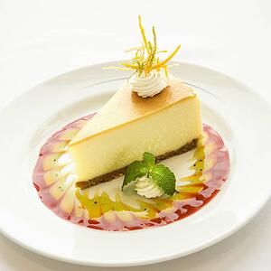 Gourmet slice of cheesecake garnished with zest and sauce and mint sprig.