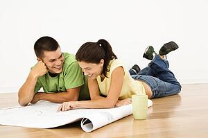 Couple lying on floor with coffee and looking at blueprints
