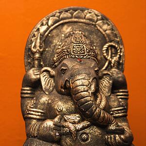 Statue of Hindu elephant Ganesha against orange wall.