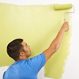 Man painting over white wall with green paint using paint roller.