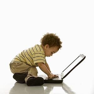 Side view of African American toddler boy using laptop computer. 