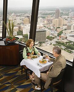 Mature couple dining in fancy restaurant by window with rooftop view of urban landscape
