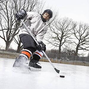 Boy in ice hockey uniform skating on ice rink moving puck