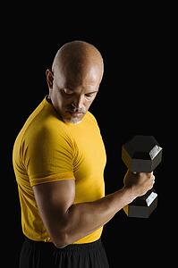 Mid adult multiethnic man wearing yellow exercise shirt doing arm curls while looking at bicep.