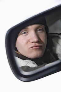 Caucasian male teenager looking at himself in side view mirror of car.