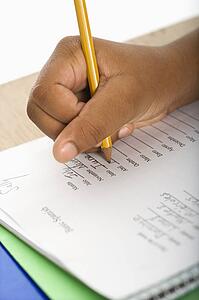 Hand of African American girl at school desk writing in notebook with pencil.