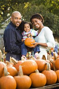 Parents and daughter picking out pumpkin and smiling at outdoor market