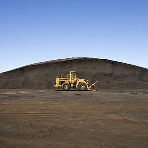 Yellow bulldozer parked beside large mound of dirt and rock.