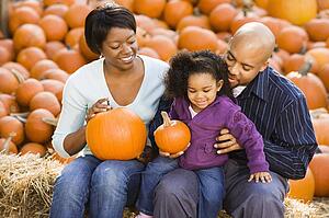 Smiling family sitting on hay bales and holding pumpkins
