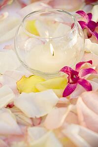 Lit candle with purple orchids and rose petals.