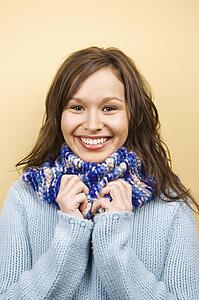 Woman wearing sweater holding hands to scarf and smiling